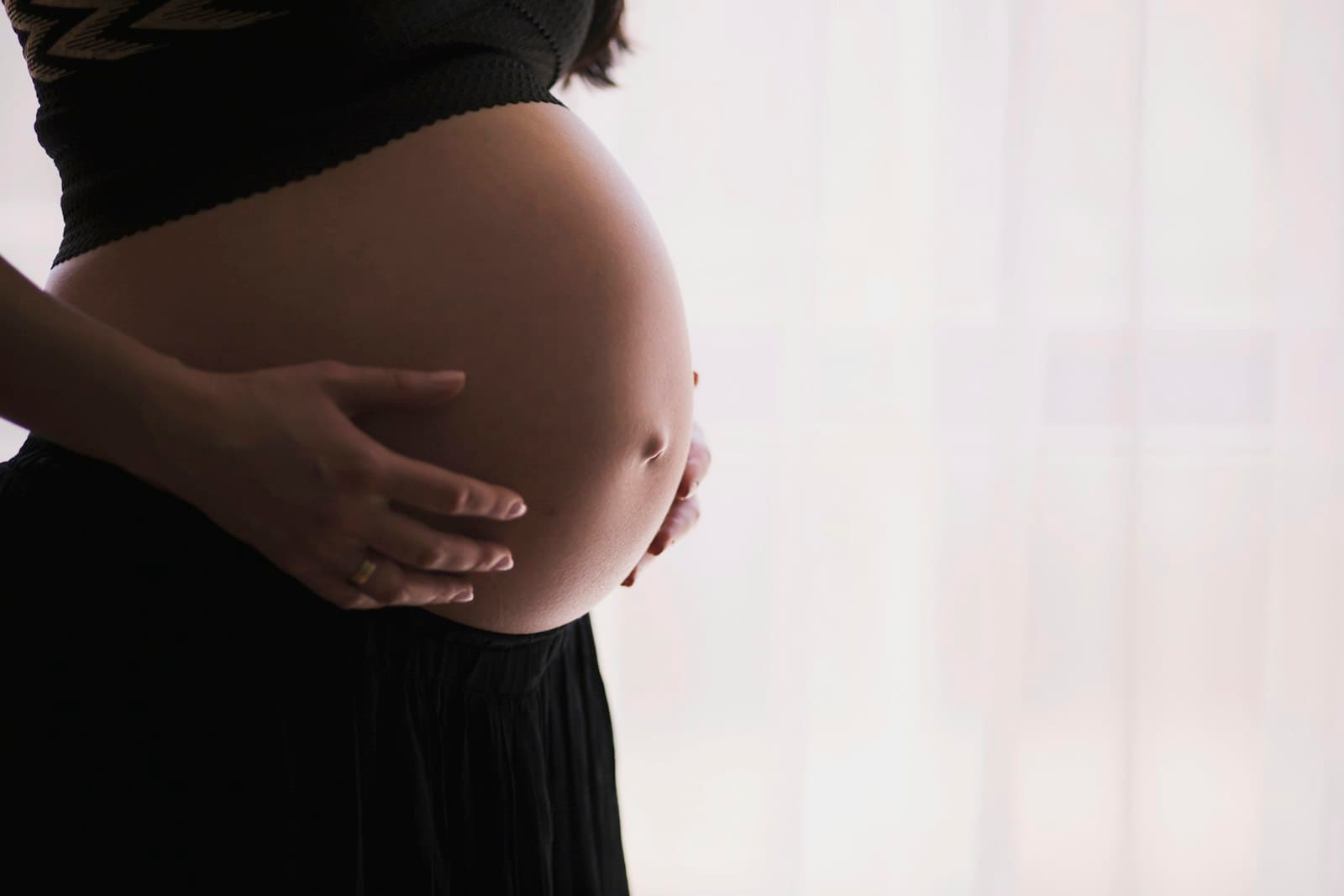 A pregnant woman gently cradling her bump in soft natural window light
