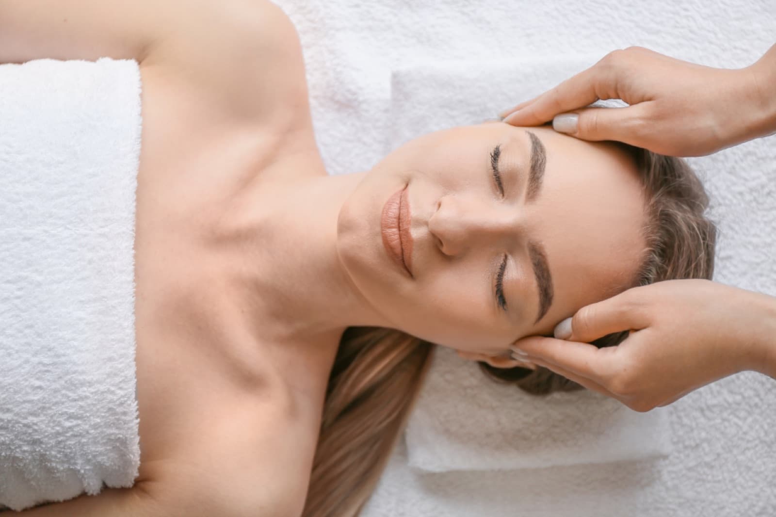 A massage therapist’s hands gently working at a relaxed client’s head and temples