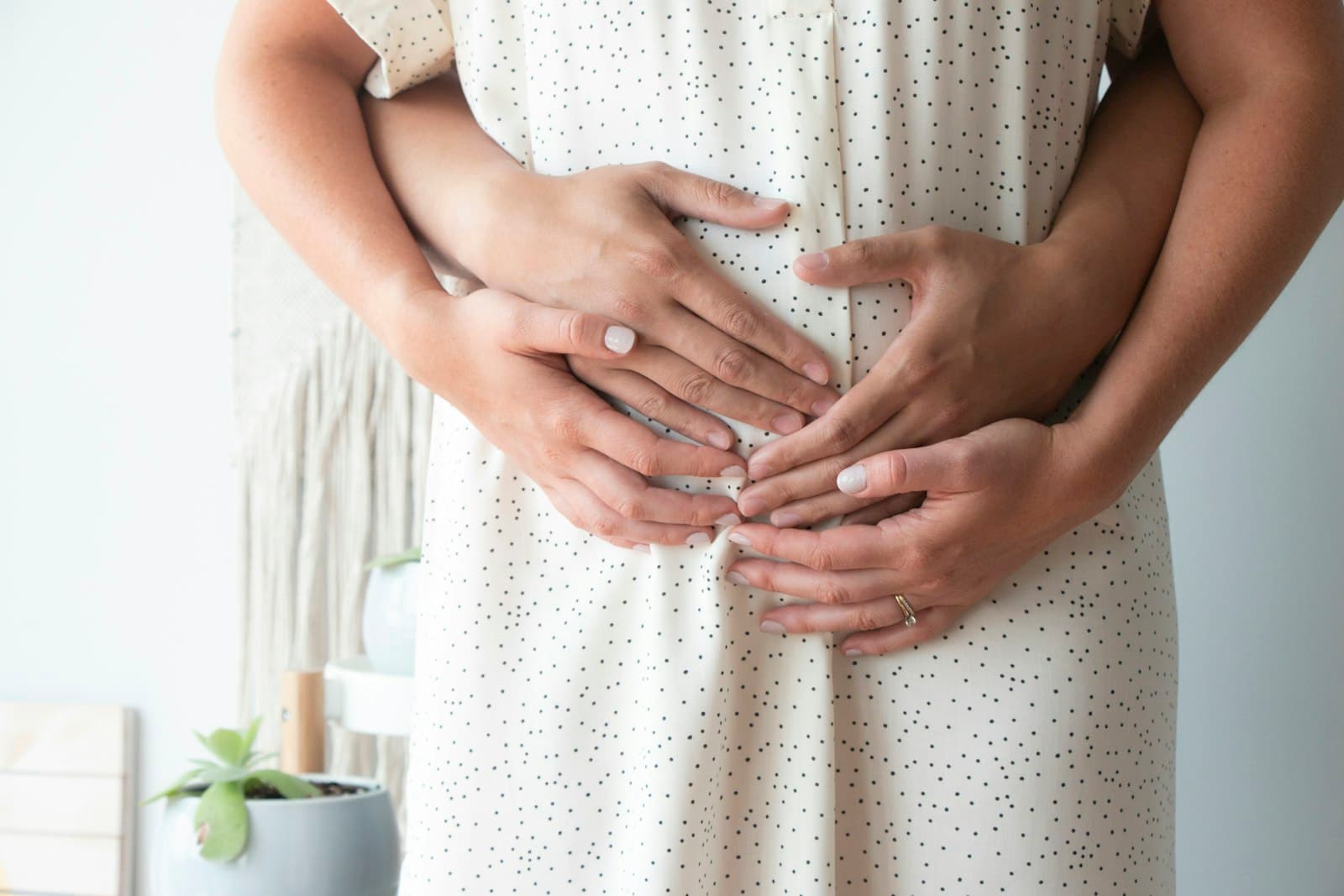 A pregnant woman supported with hands resting gently around her bump