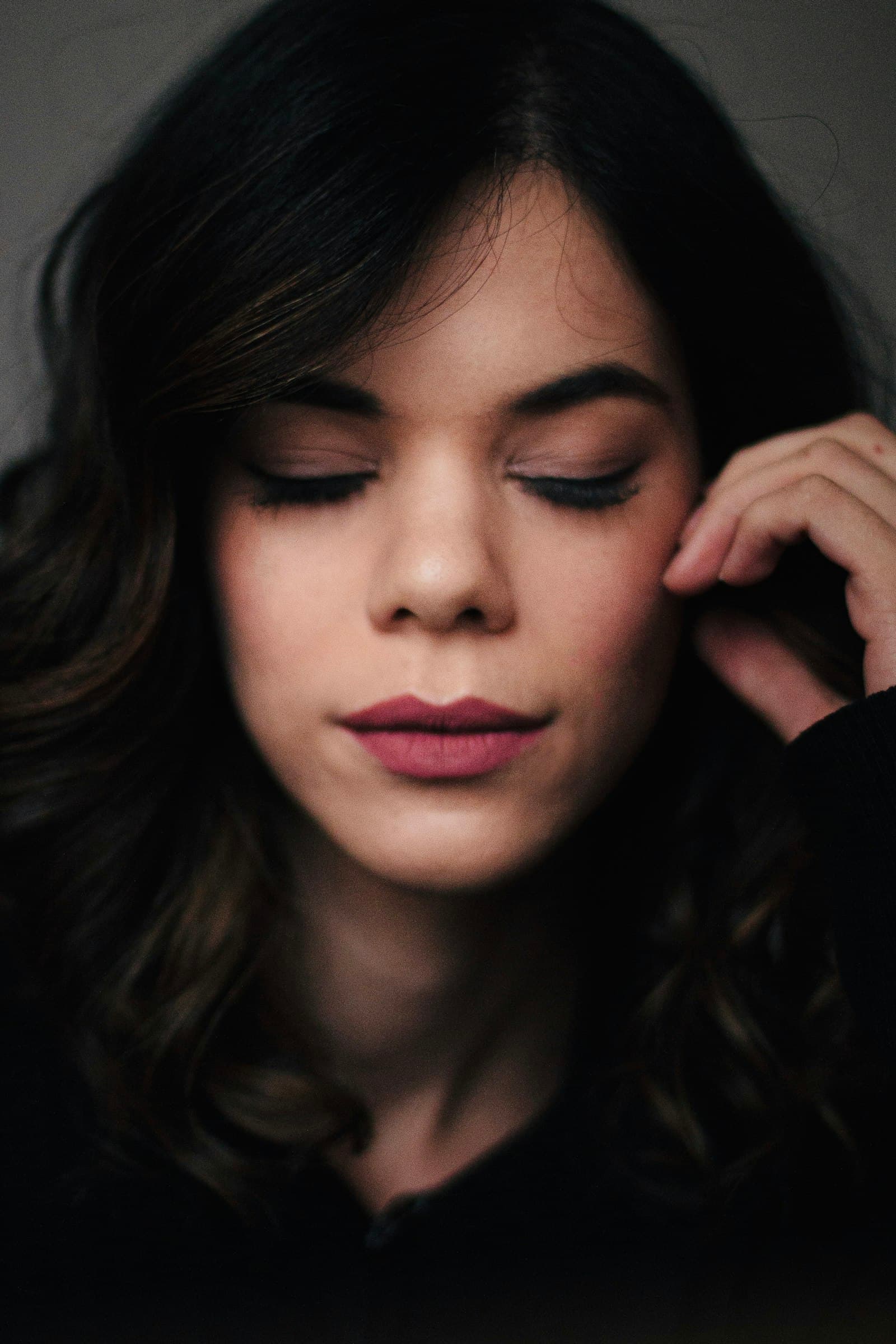 A woman sitting calmly with her eyes closed, breathing slowly in soft light