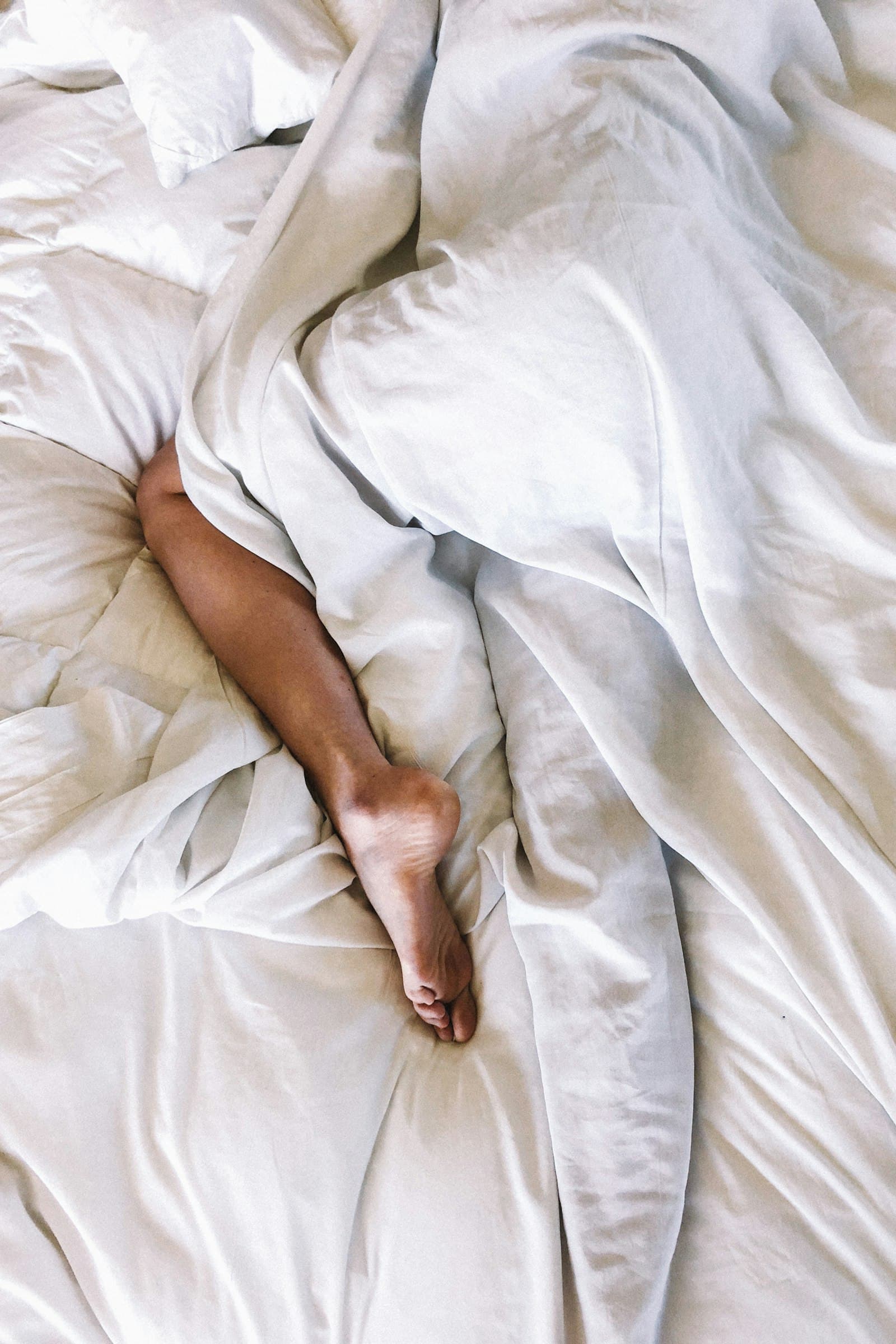 Resting legs stretched out under soft white bedding