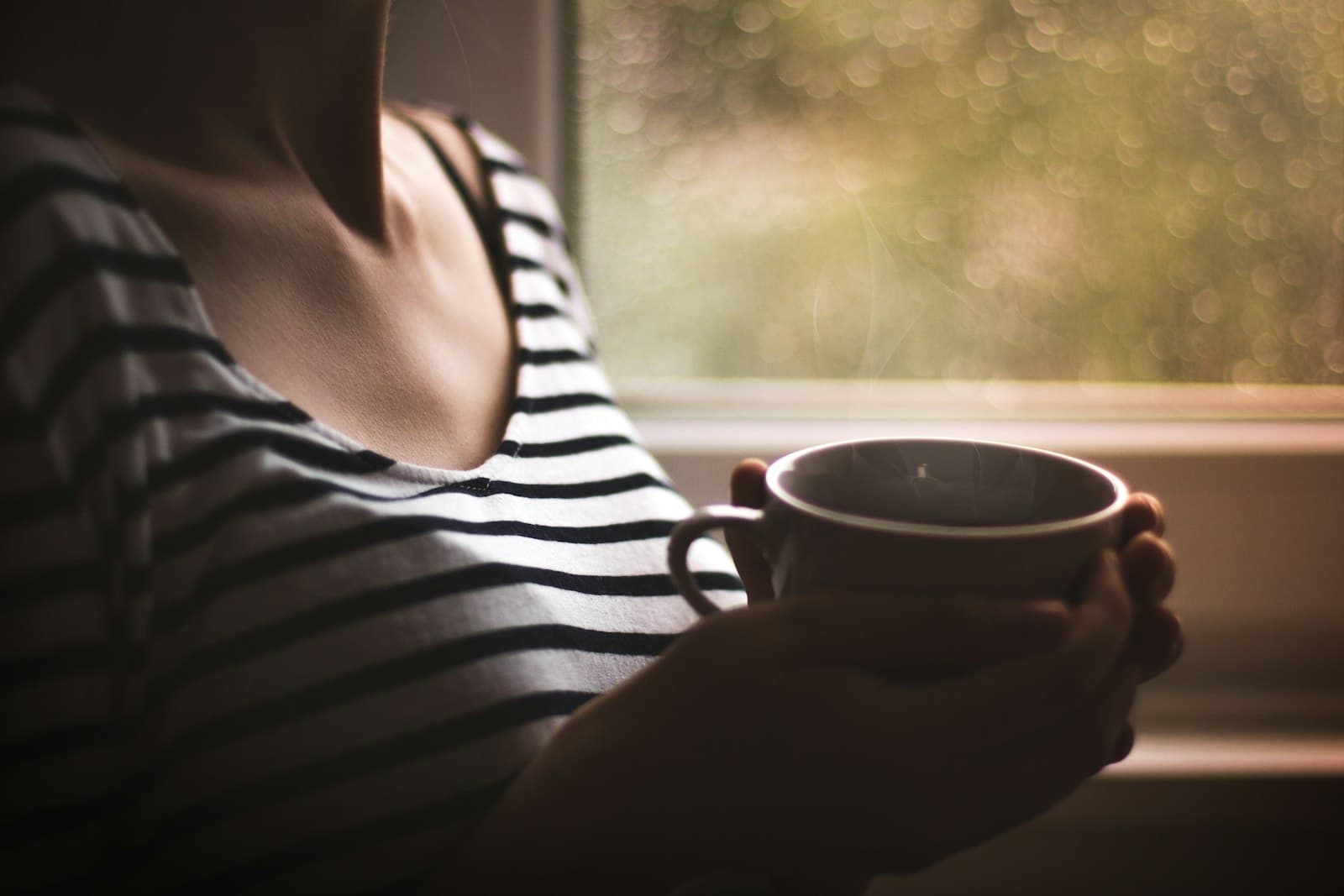 A pregnant woman resting by a window with a warm cup of tea