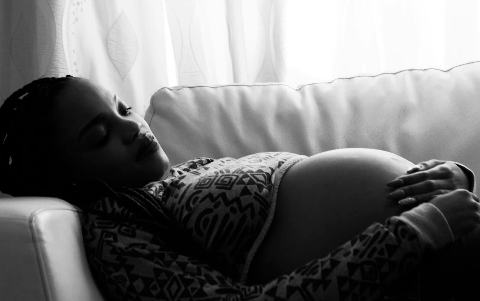 A pregnant woman resting calmly on a sofa with a hand on her bump